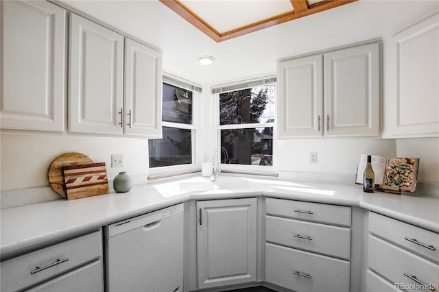 kitchen with light countertops, white dishwasher, a sink, and white cabinets