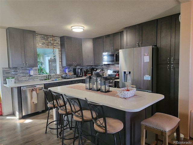 kitchen featuring sink, a breakfast bar, stainless steel appliances, a textured ceiling, and a kitchen island