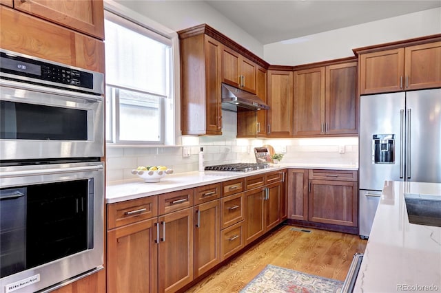 365 Casalon Pl, Superior, CO 80027 - kitchen with appliances with stainless steel finishes, under cabinet range hood, light countertops, light wood-style floors, and backsplash