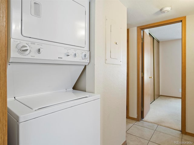 clothes washing area featuring light tile patterned floors, a textured ceiling, electric panel, and stacked washer / dryer