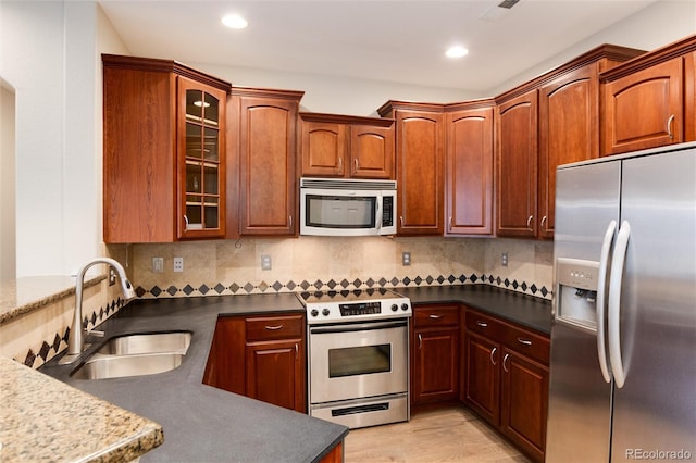 kitchen featuring sink, decorative backsplash, dark stone countertops, light hardwood / wood-style floors, and stainless steel appliances