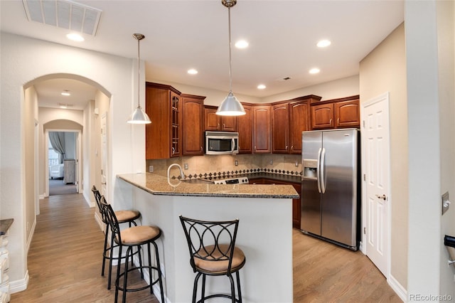 kitchen featuring kitchen peninsula, decorative backsplash, a breakfast bar, stainless steel appliances, and decorative light fixtures