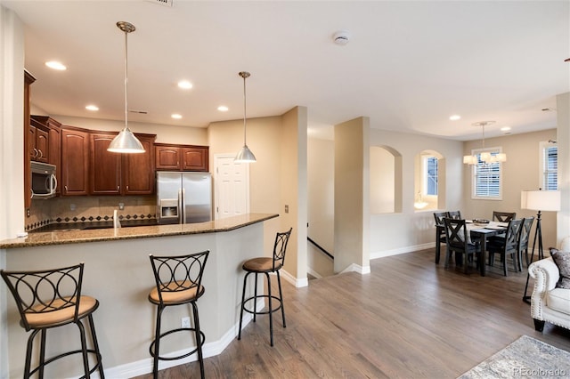 kitchen with hardwood / wood-style floors, a kitchen breakfast bar, hanging light fixtures, appliances with stainless steel finishes, and light stone counters