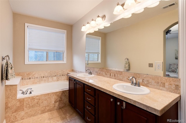 bathroom featuring plenty of natural light, ceiling fan, tiled tub, and vanity