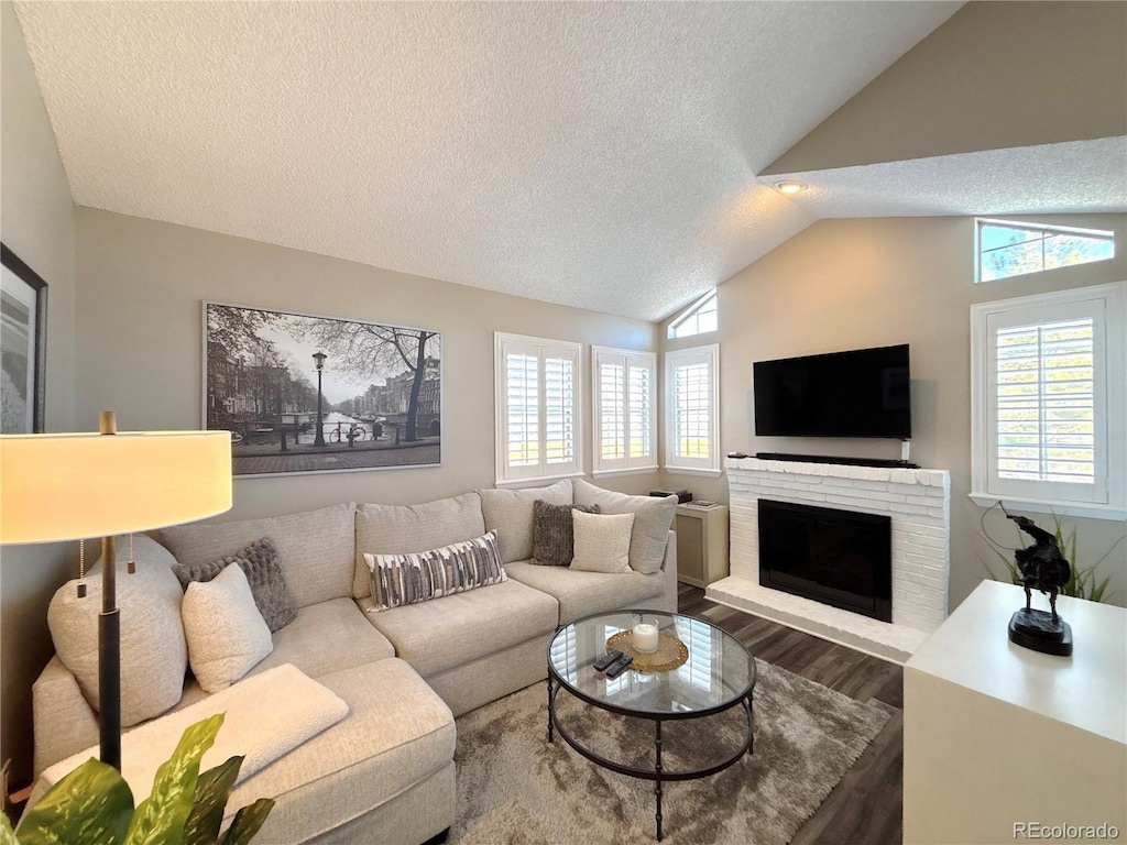 living room with dark hardwood / wood-style flooring, vaulted ceiling, a brick fireplace, and a textured ceiling