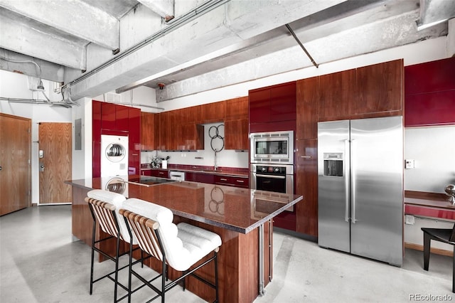 100 Park Ave Unit 2008, Denver, CO 80205 - kitchen featuring appliances with stainless steel finishes, estacked washer and dryer, concrete flooring, and a kitchen breakfast bar