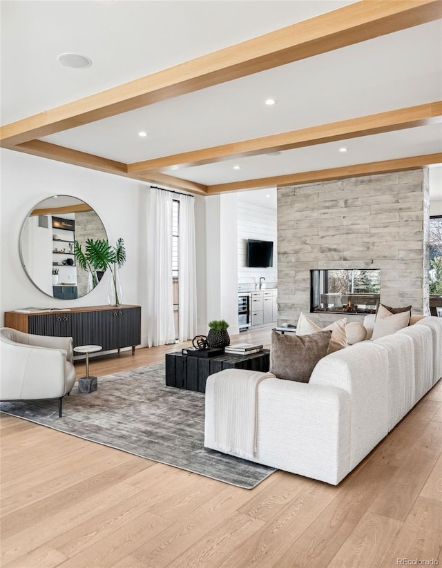 living room featuring a multi sided fireplace, beam ceiling, and light wood-type flooring