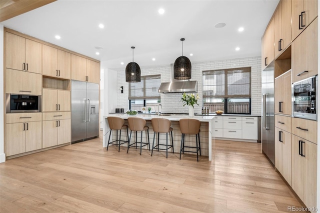 kitchen with a breakfast bar area, a center island, built in appliances, light brown cabinetry, and decorative light fixtures