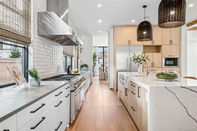 kitchen featuring pendant lighting, light brown cabinets, double oven range, light stone countertops, and wall chimney range hood