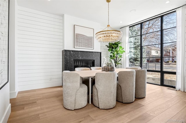 dining room featuring a wall of windows, a high end fireplace, light hardwood / wood-style flooring, and plenty of natural light