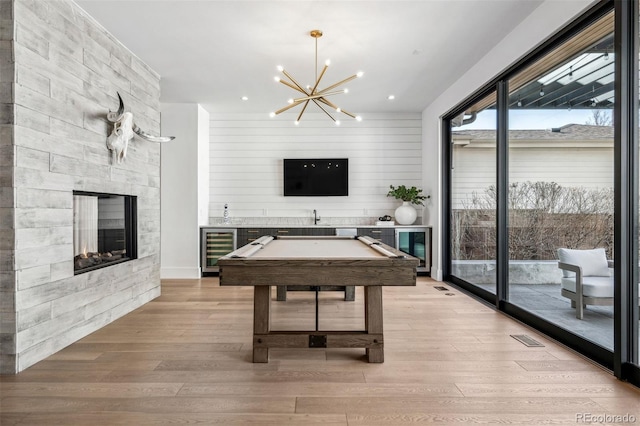 game room featuring a stone fireplace, wine cooler, and light wood-type flooring