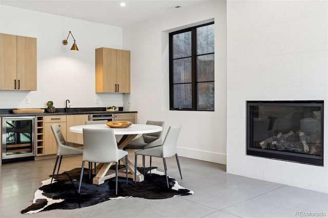 dining room with wine cooler, sink, a tiled fireplace, and concrete flooring