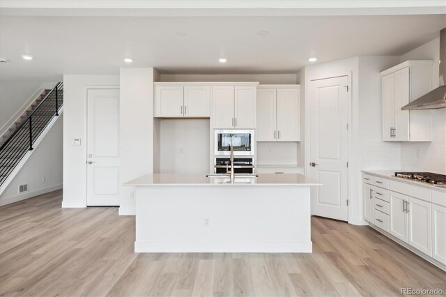 8245 Butte Creek St, Littleton, CO 80125 - kitchen featuring appliances with stainless steel finishes, a center island with sink, white cabinetry, light countertops, and light wood-type flooring