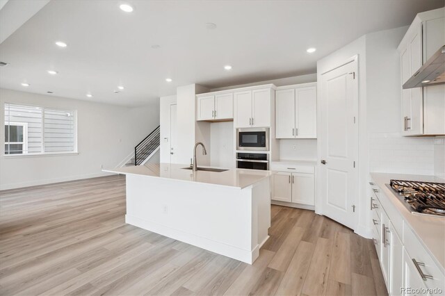 8245 Butte Creek St, Littleton, CO 80125 - kitchen with stainless steel appliances, a sink, light wood-style flooring, a kitchen island with sink, and white cabinetry