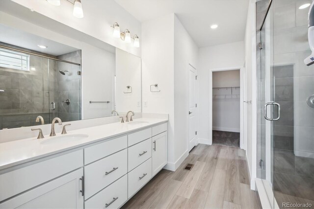 8245 Butte Creek St, Littleton, CO 80125 - full bathroom featuring double vanity, a shower stall, a walk in closet, wood finished floors, and recessed lighting