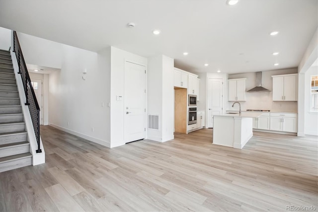 8245 Butte Creek St, Littleton, CO 80125 - kitchen with wall chimney exhaust hood, light countertops, light wood-type flooring, recessed lighting, and a center island with sink