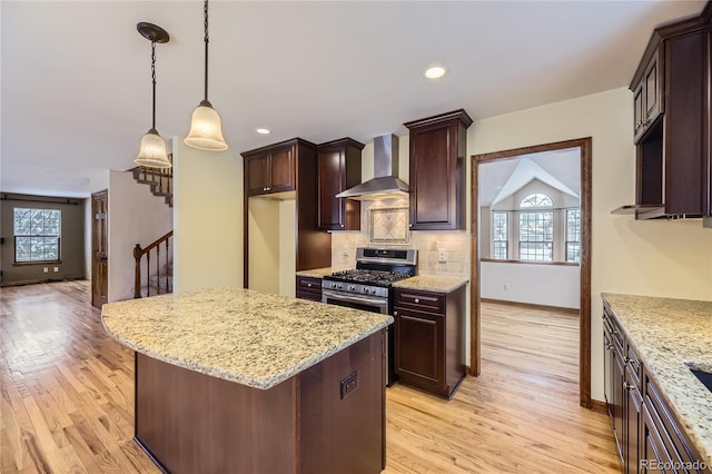 kitchen featuring a center island, stainless steel gas range oven, backsplash, wall chimney range hood, and decorative light fixtures