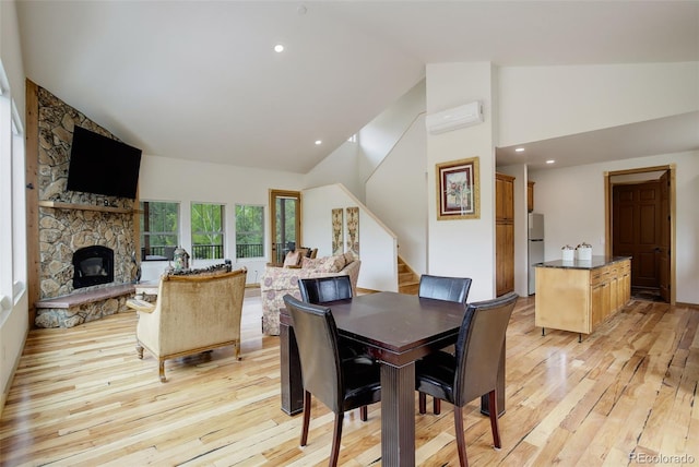 178 Cree Ct, Lyons, CO 80540 - dining space featuring light wood finished floors, a wall unit AC, high vaulted ceiling, stairs, and a stone fireplace