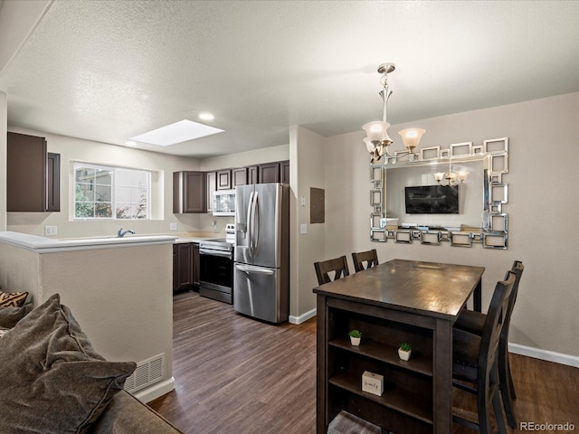 kitchen with a textured ceiling, dark wood-type flooring, a skylight, pendant lighting, and stainless steel appliances