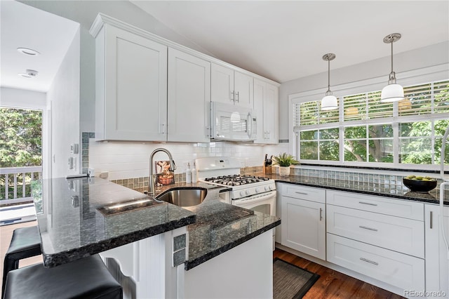 kitchen featuring sink, white appliances, a breakfast bar, white cabinetry, and vaulted ceiling