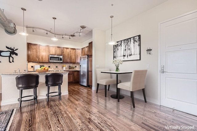 kitchen with backsplash, stainless steel appliances, a peninsula, brown cabinetry, and dark wood-style flooring