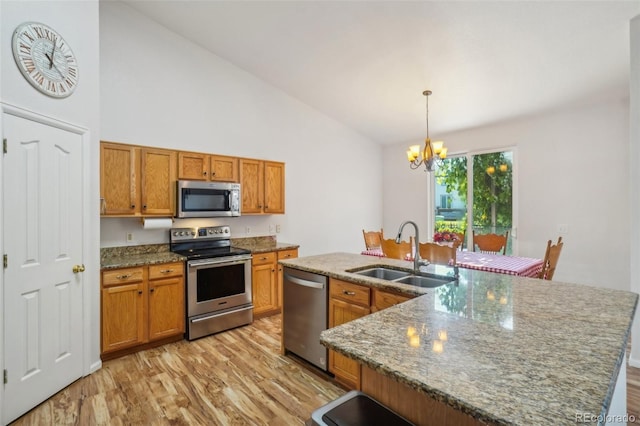 kitchen with a kitchen island with sink, stainless steel appliances, sink, light hardwood / wood-style floors, and pendant lighting