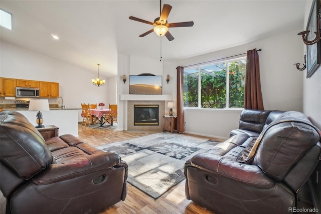 living room featuring lofted ceiling, ceiling fan with notable chandelier, a fireplace, and light hardwood / wood-style floors