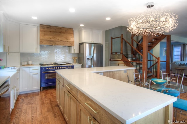 8140 S Storm King Peak, Littleton, CO 80127 - kitchen with appliances with stainless steel finishes, premium range hood, light wood finished floors, backsplash, and a chandelier