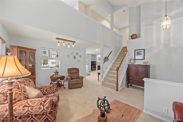 living area featuring light colored carpet, stairs, baseboards, and a towering ceiling