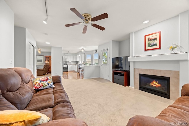 carpeted living room with ceiling fan, a tiled fireplace, and recessed lighting