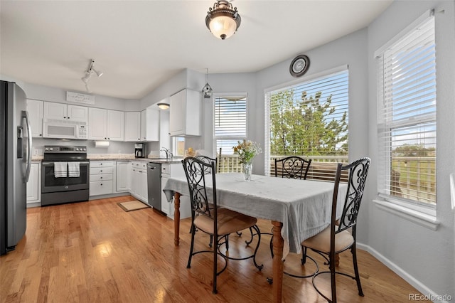 kitchen with stainless steel appliances, white cabinets, a sink, and light wood finished floors