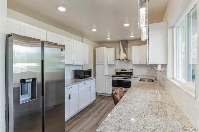 kitchen with light stone countertops, wall chimney exhaust hood, white cabinetry, a sink, and stainless steel appliances