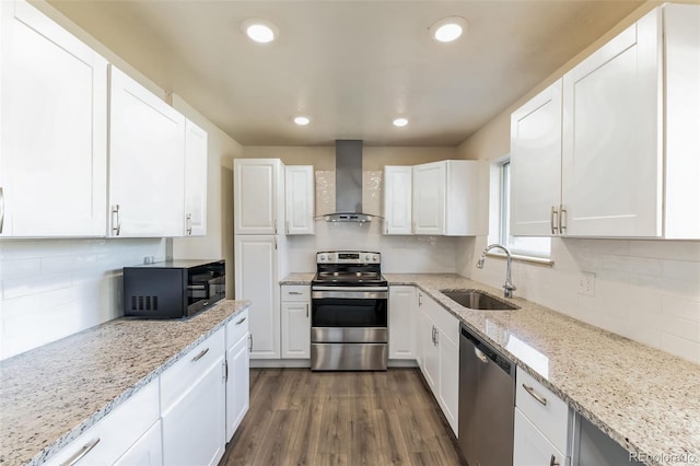 kitchen featuring wall chimney range hood, white cabinets, stainless steel appliances, and a sink