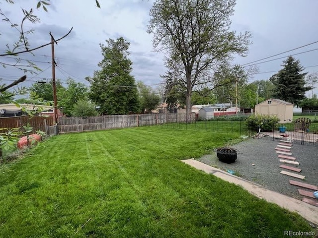 view of yard with a storage unit, a fenced backyard, an outdoor fire pit, and an outbuilding