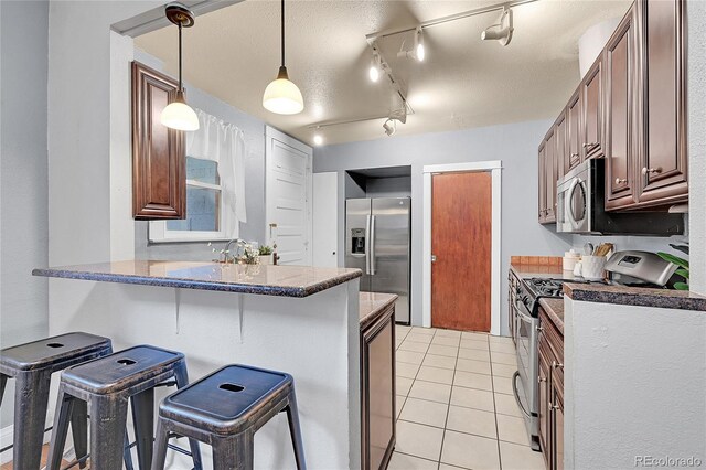 1005 S Pennsylvania St, Denver, CO 80209 - kitchen featuring appliances with stainless steel finishes, a kitchen bar, a peninsula, light tile patterned flooring, and hanging light fixtures