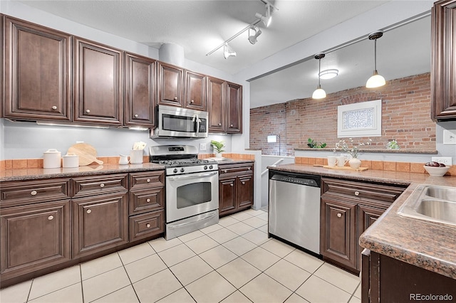 1005 S Pennsylvania St, Denver, CO 80209 - kitchen with stainless steel appliances, dark brown cabinetry, light tile patterned floors, hanging light fixtures, and brick wall