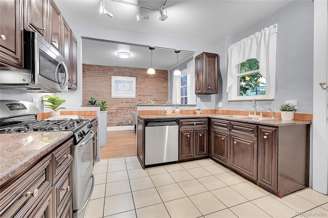 1005 S Pennsylvania St, Denver, CO 80209 - kitchen with stainless steel appliances, brick wall, dark brown cabinets, light tile patterned floors, and decorative light fixtures