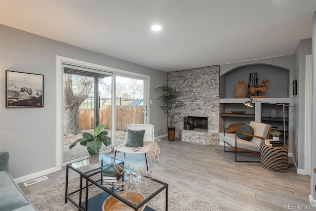 living area featuring light wood finished floors, visible vents, a stone fireplace, and baseboards