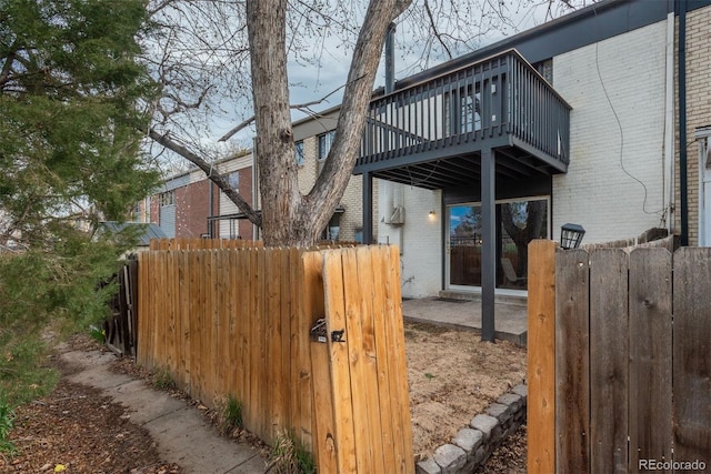 view of property exterior featuring brick siding, fence, and a deck