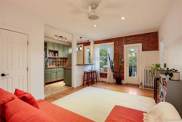 living room with light wood-type flooring, radiator heating unit, ceiling fan, and brick wall