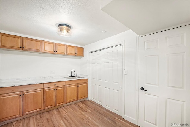 kitchen with sink, light stone counters, a textured ceiling, and light hardwood / wood-style flooring