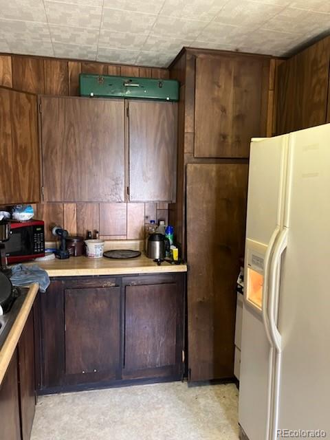 440 Colorado Ave, Stratton, CO 80836 - kitchen featuring white fridge with ice dispenser, black microwave, light countertops, and wooden walls