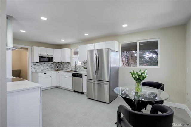 kitchen with a sink, tasteful backsplash, white cabinetry, stainless steel appliances, and light stone countertops