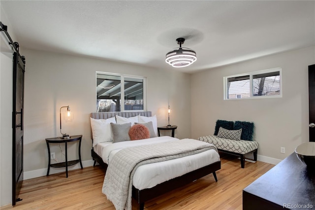 bedroom with light wood finished floors, baseboards, and a barn door