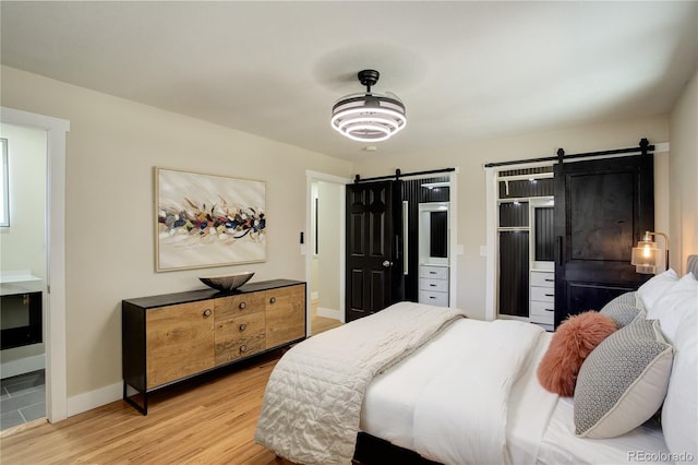 bedroom featuring baseboards, light wood-type flooring, and a barn door