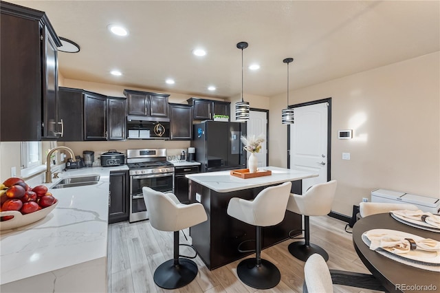 kitchen with a kitchen island, decorative light fixtures, sink, stainless steel appliances, and light stone countertops