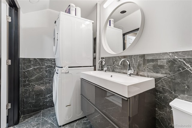 bathroom with lofted ceiling, tile walls, stacked washer / dryer, vanity, and toilet