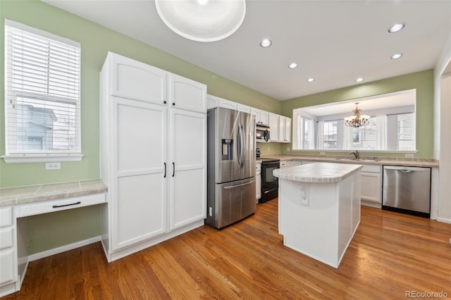 kitchen with white cabinets, stainless steel appliances, a notable chandelier, and light hardwood / wood-style floors