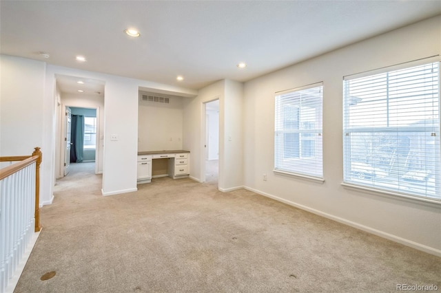 interior space with multiple windows, light carpet, and built in desk