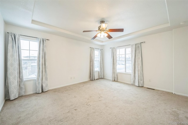 carpeted spare room with a raised ceiling, a wealth of natural light, and ceiling fan